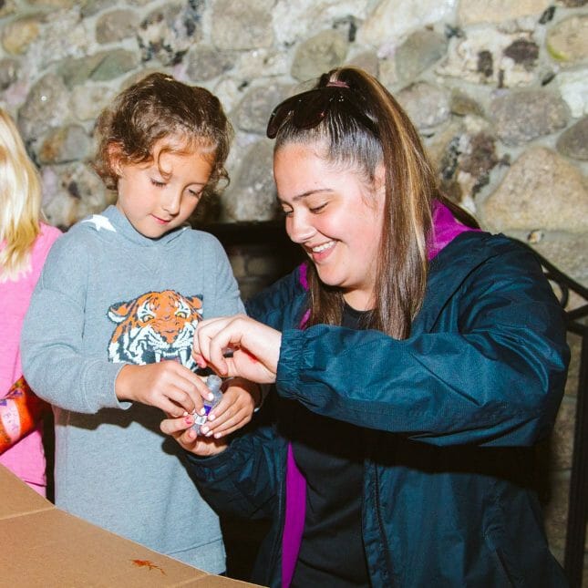 Staff helping a female camper at arts and crafts