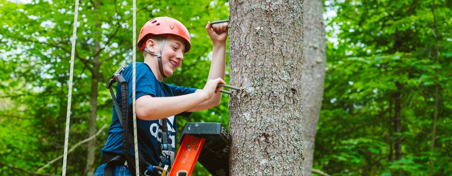 Male camper climbing ladder and tree to high ropes course