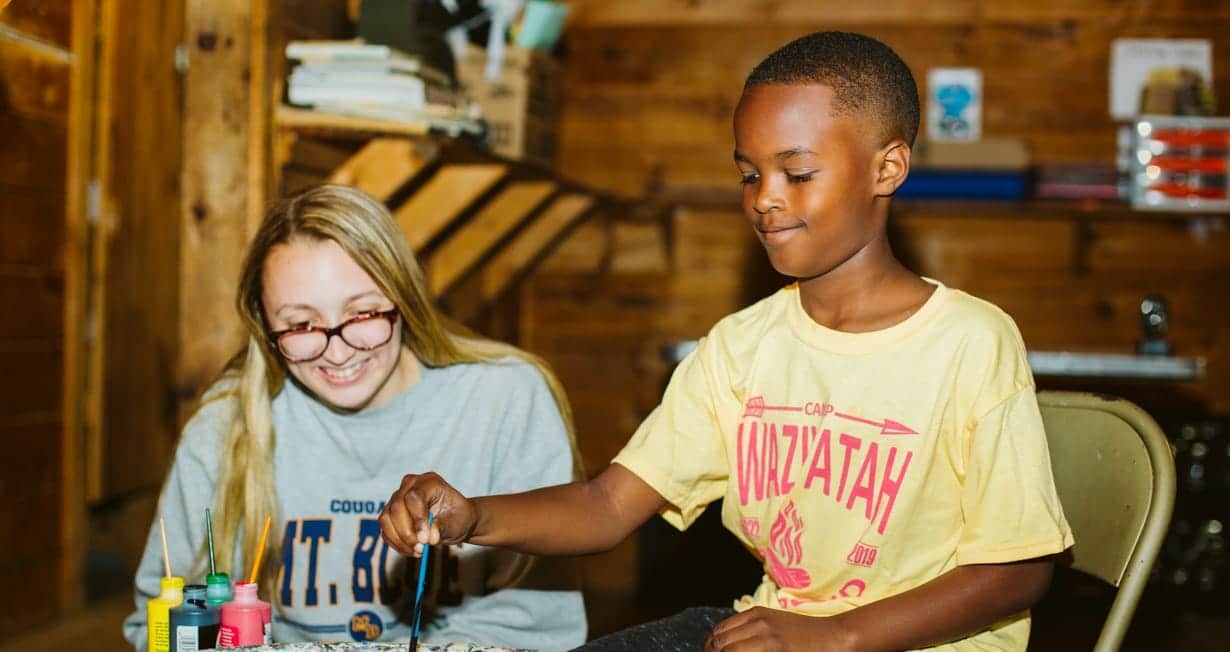 Arts and crafts instructor teaching a camper how to use the pottery wheel