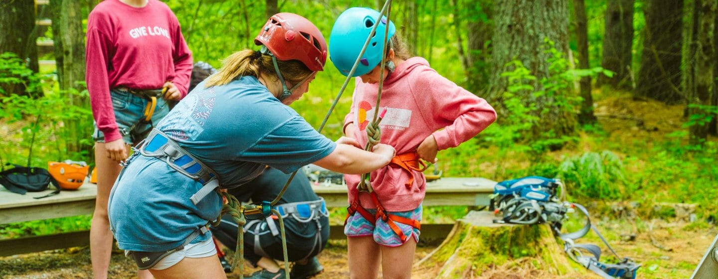 Staff helping camper put her climbing harness on