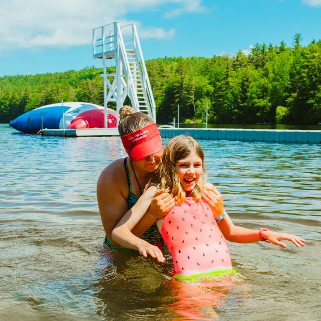 Lifeguard helping camper learn how to swim in lake