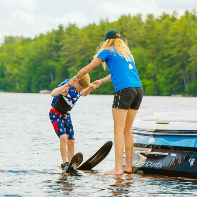 Staff helping a camper with water skiing